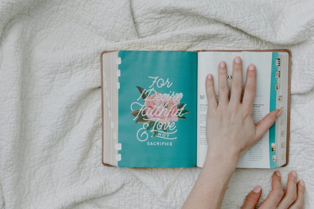 pexels-photo-8383458-8383458 An open Bible on a white quilt with a hand resting on the page, promoting faith and reflection.
